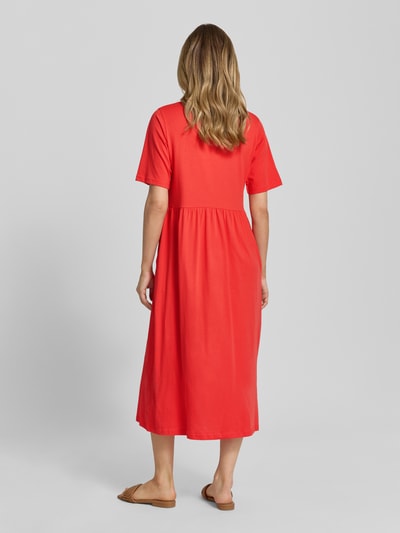 Frauenmodel trägt Midikleid mit Smok-Details Modell 'DERBY' von Soyaconcept in Koralle, reine Baumwolle, A-Linie, Ganzkörperansicht Rückansicht.