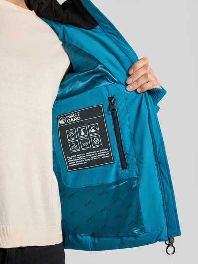 Frauenmodel trägt Jacke mit Daumenloch und Kapuze von NAUTGÅRD in Blau, glatte Textur, Zweiwege-Reißverschluss, Nahaufnahme Oberkörper.