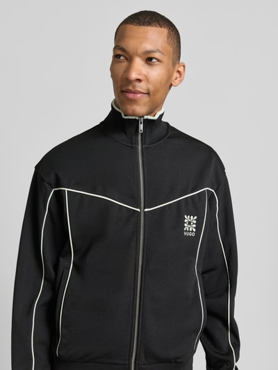 Männermodel trägt Relaxed Fit Sweatjacke aus Baumwoll-Mix Modell 'DARYNT' von HUGO, mehrfarbige Optik, Kontraststreifen, Logo-Stitching, Reißverschluss, seitliche Eingrifftaschen, gerippte Ärmelabschlüsse und Rumpfabschluss, Nahaufnahme Oberkörper.