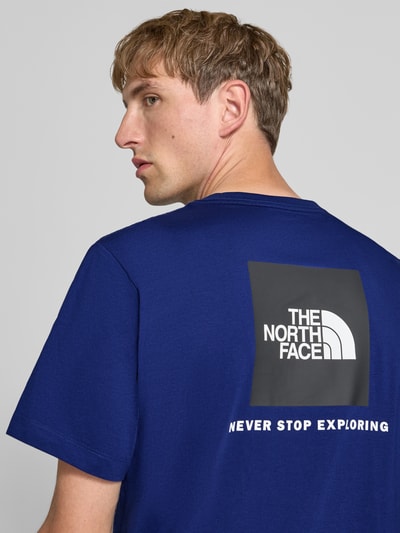 Männermodel trägt donkerblauw t-shirt van katoenmix met witte labelprint Model 'Evolution' van The North Face, regular fit, ruglengte bij maat M 73 cm, nahaufnahme bovenlichaam