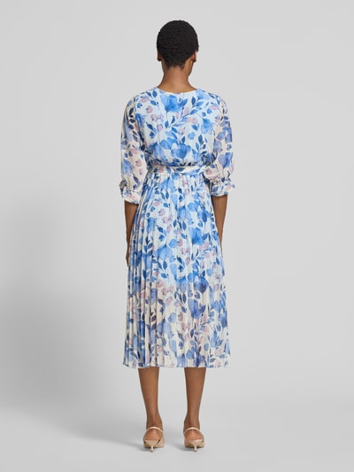 Frauenmodel trägt Midikleid im Allover-Look mit Bindegürtel von ZABAIONE, A-Linie, florale Muster in Blau und Weiß, Ganzkörperansicht Rückansicht.