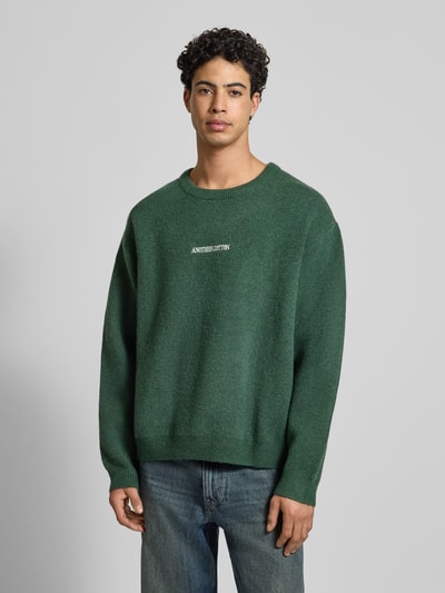 Männermodel trägt Strickpullover mit gerippten Abschlüssen von ANOTHER COTTON LAB, Material-Mix, lockerer Schnitt, Rundhalsausschnitt, Label-Stitching, Ganzkörperansicht von vorne.
