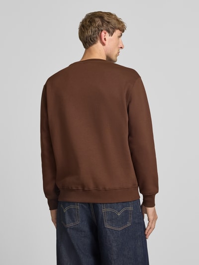 Männermodel trägt Regular Fit Sweatshirt aus Baumwoll-Mix mit Label-Detail von Alpha Industries in Braun, Ganzkörperansicht Rückansicht. Herren Sweatshirt, elastische Abschlüsse, Rückenlänge 67 cm, Ärmellänge 63 cm.