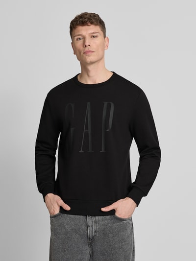 Männermodel trägt Sweatshirt mit Rundhalsausschnitt und Logo von GAP, schwarz, Baumwoll-Mix, Regular-Fit, Ganzkörperansicht von vorne.