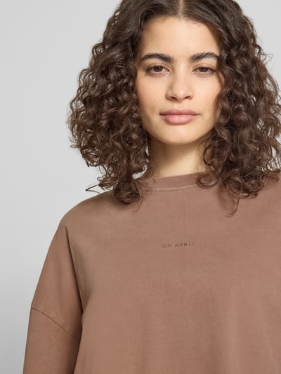Modelka nosi Regular Fit Sweatshirt mit Label-Detail od OH APRIL z bawełny, okrągły dekolt, detal z logo, kolor brązowy, zbliżenie górnej części ciała.