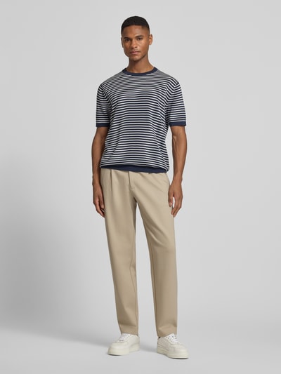 Männermodel trägt Hose mit französischen Eingrifftaschen von CK Calvin Klein aus Baumwoll-Mix mit Stretch-Anteil, Tapered-Fit, beige, Ganzkörperansicht von vorne.