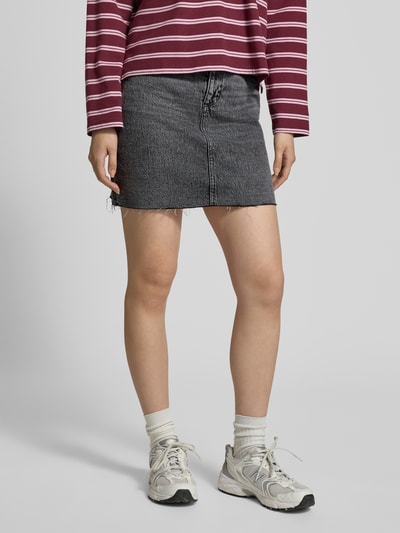 Frauenmodel trägt Regular Fit Jeansrock aus Baumwoll-Mix Modell 'TESSA' von Vero Moda in Denim-Optik mit 5-Pocket-Design, Mini-Länge, Label-Patch, Gürtelschlaufen, Knopf und verdecktem Reißverschluss, Materialverarbeitung Twill; Nahaufnahme Unterkörper von vorne.