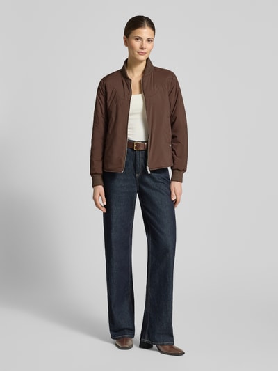 Vrouwenmodel draagt Regular Fit Bomberjacke mit Stehkragen van Scotch & Soda in bruin met steekzakken, ritssluiting, elastische boorden, ganzebodyvooraanzicht. Ruglengte maat S: 57 cm, schouderbreedte: 36 cm, borstwijdte: 48 cm, mouwlengte: 62 cm.