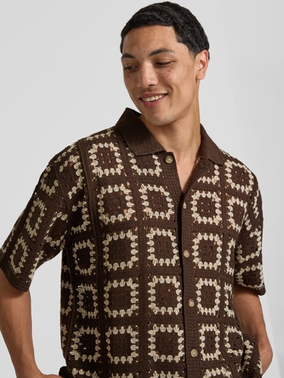 Männermodel trägt Regular Fit Freizeithemd im Allover-Look Modell 'FABIAN' von Redefined Rebel, braun mit beige Muster, Knopfleiste, Polokragen, Nahaufnahme Oberkörper. Rückenlänge bei Größe M: 70 cm, Schulterbreite: 43 cm, Ärmellänge: 28 cm.
