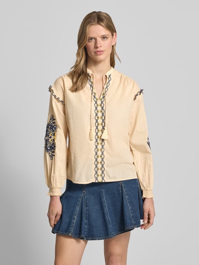 Frauenmodel trägt Loose Fit Tunika aus reiner Baumwolle Modell 'BELIZA' von Pepe Jeans in Beige mit floralem Stitching, Popeline-Textur, schwarze und blaue Akzente, tiefer V-Ausschnitt, gesmokte Ärmelbündchen, unifarbene Optik, Ganzkörperansicht von vorne.