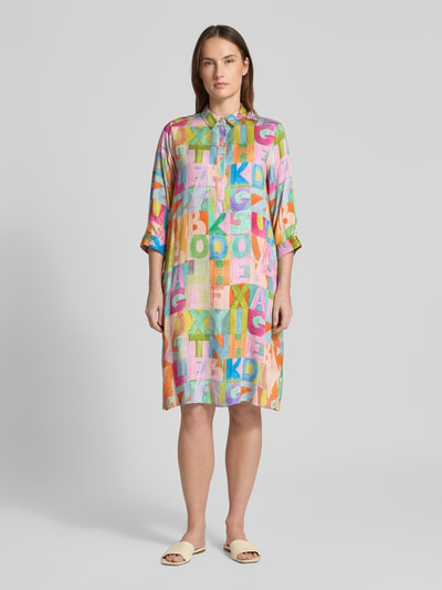 Modelka kobieta nosi Relaxed Fit Hemdblusenkleid aus reiner Viskose od Milano Italy, kolorowy nadruk liter, długość do kolan, widok z przodu całej sylwetki. Context: sukienka koszulowa damska, czysta wiskoza, krój relaxed fit, kołnierz koszulowy, zapięcie na guziki, rękaw 3/4, nadruk na całej powierzchni, długość tyłu w rozmiarze 36: 97 cm, szerokość w rozmiarze 36: 48 cm, długość rękawa w rozmiarze 36: 43 cm.