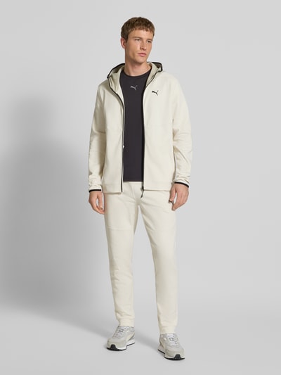 Männermodel trägt Sweatjacke mit Kapuze von PUMA PERFORMANCE aus Baumwoll-Mix, Lockerer-Schnitt, helle Farbe, mit Reißverschluss, Label-Print und Eingrifftaschen, Ganzkörperansicht von vorne.
