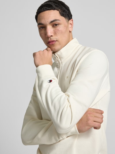Männermodel trägt Sweatshirt mit Stehkragen und Reißverschluss von CHAMPION in Creme, Baumwoll-Mix, Label-Stitching, Nahaufnahme Oberkörper.