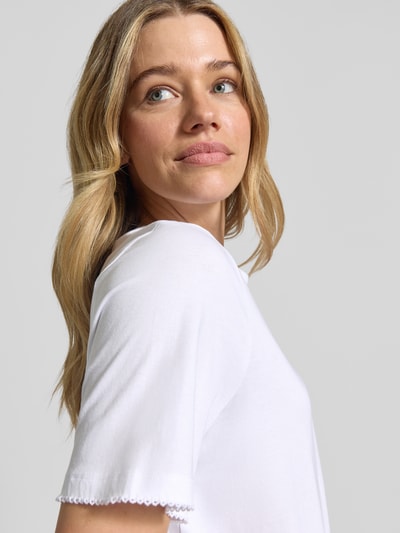 Kobiece modelka nosi Regular Fit T-Shirt aus reiner Baumwolle Modell 'ASSIA' od Selected Femme, jednokolorowy jersey z ozdobnymi szwami, jasny materiał, krótki rękaw, okrągły dekolt, detaliczne tekstury, zbliżenie na górną część ciała.