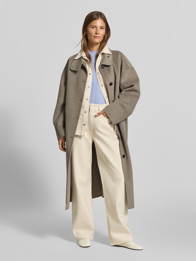 Frauenmodel trägt Slim Fit Pullover mit Woll-Anteil von MYON, hellblau mit Lochmuster, Stehkragen, kombiniert mit hellem Mantel, Ganzkörperansicht von vorne.