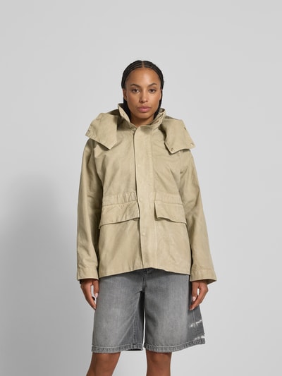 Frauenmodel trägt Jacke aus reiner Baumwolle mit Kapuze von Victoria Beckham in Beige, lockere Passform, seitliche Eingrifftaschen, durchgehende Reißverschluss und Knopfleiste, Rückenlänge 67 cm, Brustweite 74 cm, Ärmellänge 56 cm, Ganzkörperansicht von vorne.