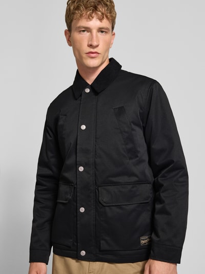 Männermodel trägt Regular Fit jack in stiksels van JACK & JONES, zwarte kleur, met platte kraag in corduroy look, opgestikte zakken, logopatch, Nahaufnahme Oberkörper. Ruglengte maat M 72 cm, schouderbreedte 49 cm, borstwijdte 59 cm, mouwlengte 65 cm.