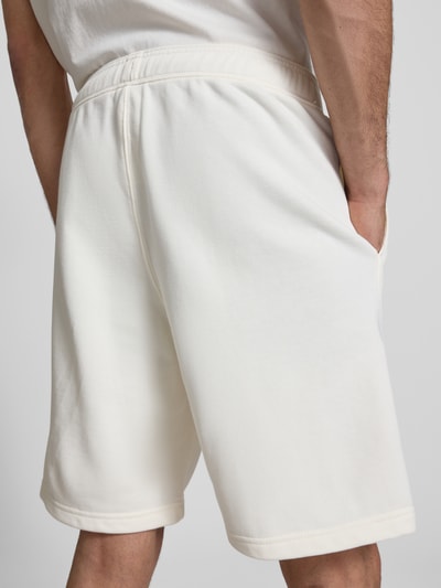 Männermodel trägt Bermudas mit elastischem Bund und Label-Stitching von CHAMPION aus Baumwoll-Mix in Weiß, Ganzkörperansicht Rückansicht. Regular-Fit mit Längsnähten, Bundweite bei Größe M 42 cm, Innenbeinlänge 24 cm.