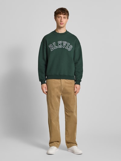 Männermodel trägt Sweatshirt mit Logo und Rundhalsausschnitt von BLKVIS, Reine Baumwolle, Relaxed-Fit, dunkelgrün, Ganzkörperansicht von vorne.