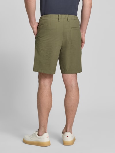 Męski model nosi Regular Fit Bermudas aus Baumwoll-Mix Modell 'KARL' von SELECTED HOMME, efekt: wzór w paski, mieszanka bawełny, krój regular fit, wpuszczane kieszenie, elastyczny ściągacz, szlufki na pasek, zapięcie na guzik i zamek błyskawiczny, faktura seersucker, kolor oliwkowy, Ganzkörperansicht Rückansicht