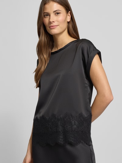 Frauenmodel trägt T-Shirt mit Rundhalsausschnitt Modell 'ELLETTE' von Vila aus schwarzem Satin mit Spitzenbesatz, Nahaufnahme Oberkörper.