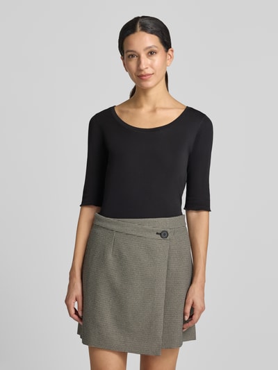 Modelka kobieca ma na sobie T-Shirt mit Ärmelaufschlag und Rundhalsausschnitt von Marc Cain, mieszanka bawełny z dodatkiem streczu, dopasowany krój, okrągły dekolt, rękawy z zakładką, detal z logo, długość tyłu w rozmiarze 36: 60 cm, ujęcie całej sylwetki z przodu.