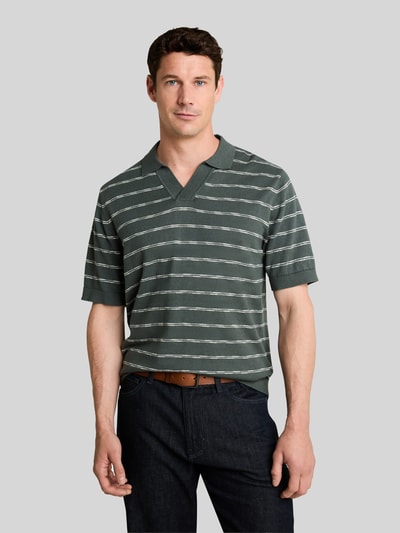 Männermodel trägt Regular Fit Poloshirt aus reiner Baumwolle von Tom Tailor in Dunkelgrün mit weißen Streifen, Ganzkörperansicht von vorne.