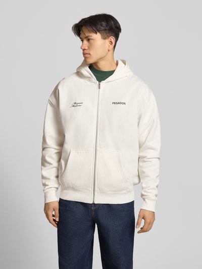 Männermodel trägt Oversized Sweatjacke mit Label-Print Modell 'Rochefort' von Pegador aus Baumwoll-Mix in Creme mit Kapuze, Reißverschluss, Eingrifftaschen, Ganzkörperansicht von vorne.