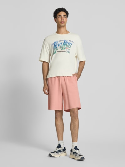 Männermodel trägt Regular Fit Shorts mit Strukturmuster von KARL KANI aus Baumwoll-Mix in Rosa mit Logo-Stitching, elastischer Bund, Ganzkörperansicht von vorne.