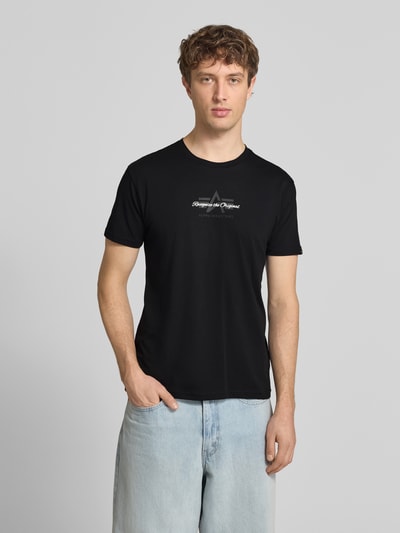 Männermodel trägt Slim Fit T-Shirt aus reiner Baumwolle von Tommy Jeans in Optik: Unifarben mit Label-Print und Logo-Stitching, Ganzkörperansicht von vorne.