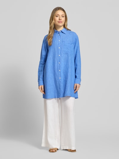 Frauenmodel trägt Relaxed Fit Longbluse aus Leinen Modell 'TAHIA' von 0039 Italy in Blau mit Hemdblusenkragen, Knopfleiste, Brusttasche, Ganzkörperansicht von vorne, Rückenlänge 86 cm, Ärmellänge 58 cm, reine Leinen-Textur.
