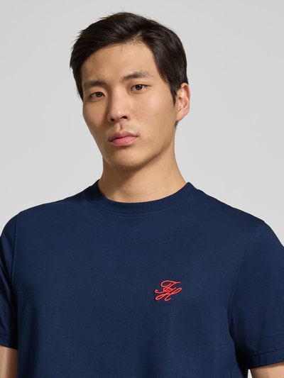 Männermodel trägt Regular Fit T-Shirt aus reiner Baumwolle von Tommy Hilfiger, unifarben dunkelblau, Logo-Stitching, Nahaufnahme Oberkörper.