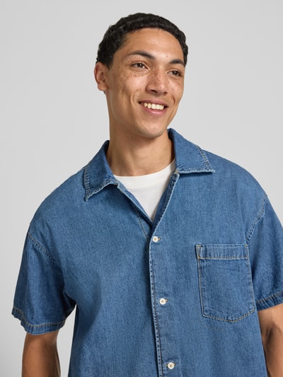 Männermodel trägt Modern Fit jeanshemd met borstzak model 'AUSTIN' van Jack & Jones in blauwe gewaxte katoen, nahaufnahme bovenlichaam, context: heren jeanshemd, kentkraag, knoopsluiting, ruglengte maat M 66 cm, schouderbreedte maat M 55 cm, mouwlengte maat M 22 cm.