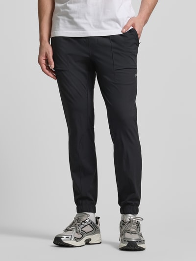 Männermodel trägt schwarze Slim Fit Sweatpants mit Logo-Print von Fabletics, Reißverschlusstaschen, elastischem Bund, Ganzkörperansicht von vorne.