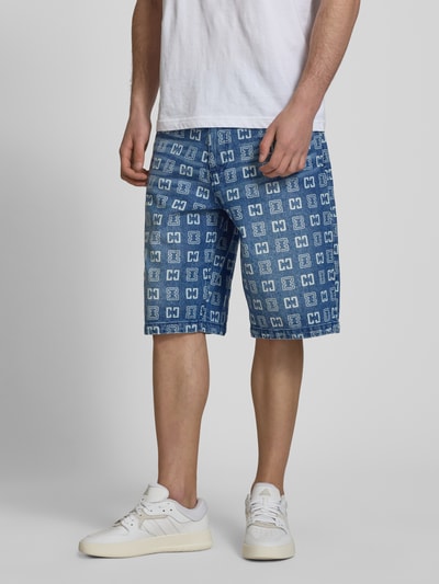 Männermodel trägt Straight Fit Jeans in Denim-Optik mit Allover-Logo-Print von COLUCCI, 5-Pocket-Design, reine Baumwolle, Ganzkörperansicht von vorne.