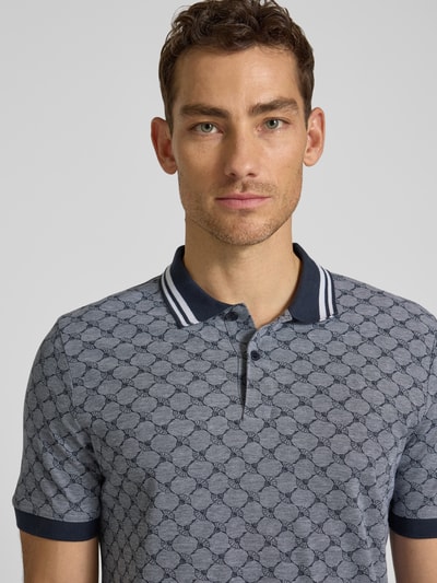 Mężczyzna nosi Regular Fit Poloshirt mit Logo-Muster Modell 'Jessino' von JOOP! Collection z czystej bawełny, krótki rękaw, ciemnoniebieskie i szare odcienie, guziki, krój regular fit, detaliczny wzór logo, widoczne szwy, długość tyłu przy rozmiarze M: 69 cm, nahaufnahme górnej części ciała