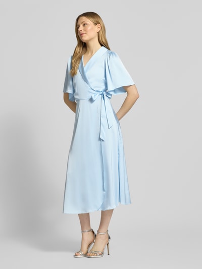 Vrouwenmodel draagt lichtblauwe satijnen midi-jurk in wikkellook van model 'VIENNA RAVENNA' van Vila, getailleerd model, V-hals, ganzekörperaanzicht van voren.