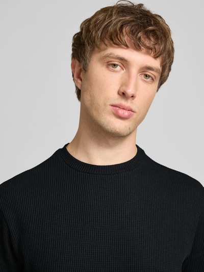 Männermodel trägt Regular Fit T-Shirt aus Baumwoll-Mix Modell 'TOBIE' von Only & Sons in Schwarz mit Waffel-Struktur, Nahaufnahme Oberkörper.