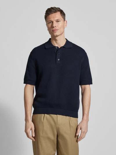 Männermodel trägt Relaxed Fit Poloshirt aus reiner Baumwolle Modell 'DANE' von SELECTED HOMME in Dunkelblau, Strickoptik, Ganzkörperansicht von vorne.
