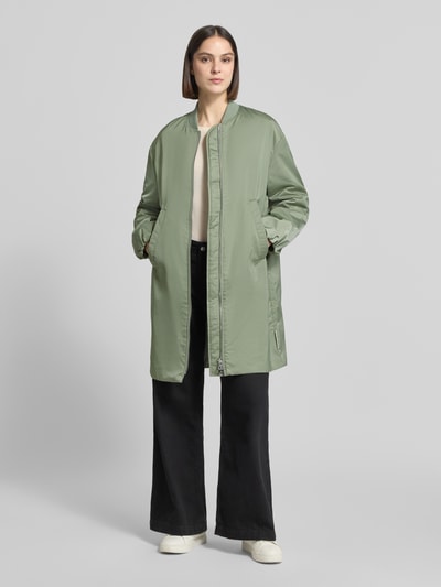 Kobiece modelka nosi Regular Fit Blouson-Mantel mit College-Kragen von Marc O'Polo, efekt: jednolity kolor, krój regular fit, kształt kołnierza: kołnierz college, zapięcie: zamek błyskawiczny dwustronny, aplikacja: naszywka z logo, rękawy: długi rękaw, zakończenie rękawów: elastyczny, wpuszczane kieszenie boczne, kieszeń wewnętrzna, wykończenie materiału: satyna, jasna zieleń, prostokątne kształty, gładka tekstura, Ganzkörperansicht von vorne.
