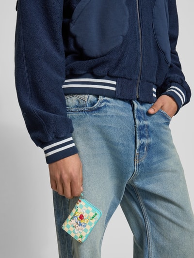 Männermodel trägt Portemonnaie mit Rundum-Reißverschluss von Kenzo mit Motiv-Print und Label-Details, Nahaufnahme Oberkörper.