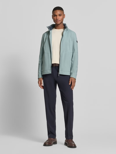 Männermodel trägt Regular Fit Jacke mit Stehkragen von bugatti in hellem Blau mit Logo-Detail, Zweiwege-Reißverschluss und Eingrifftaschen, elastische Ärmelabschlüsse, verstaubare Kapuze, Regular Fit, Rückenlänge 68 cm, Schulterbreite 42 cm, Brustweite 50 cm, Ärmellänge 65 cm, Ganzkörperansicht von vorne.
