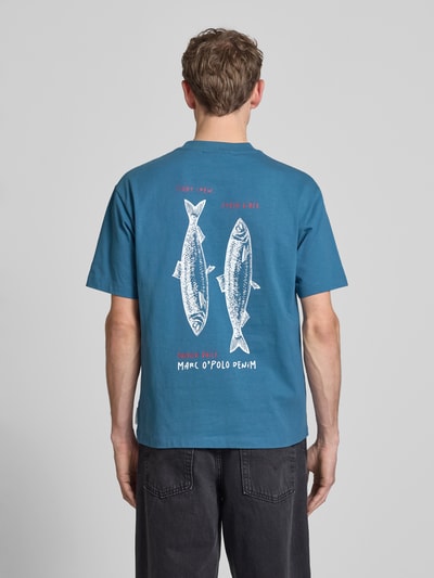 Männermodel trägt Relaxed Fit T-Shirt aus reiner Baumwolle von Marc O'Polo Denim in Blau, Motiv-Print und Label-Print, Ganzkörperansicht Rückansicht.
