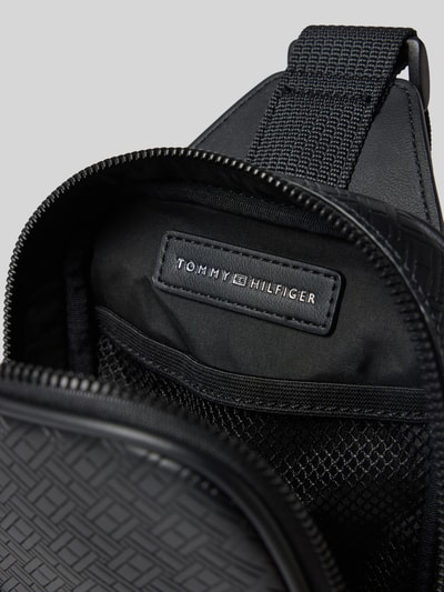 Produktfoto, Umhängetasche mit Logo-Detail Modell 'EMBOSSED FLAG SLING' von Tommy Hilfiger, czarny kolor, imitacja skóry, wzór wytłoczony, detal z logo, zamek błyskawiczny, główna przegroda, przegródka zapinana na zamek błyskawiczny, przegródka z siateczki, wykończenie materiału ze sztucznej skóry