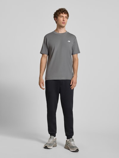 Männermodel trägt T-Shirt mit Logo und Rundhalsausschnitt von New Balance in Grau, reine Baumwolle, Regular Fit, Ganzkörperansicht von vorne.