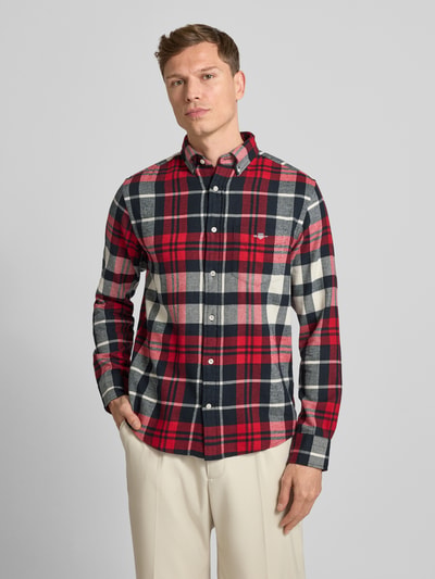 Männermodel draagt Gant Vrijetijdsoverhemd van puur katoen met regular fit, button-downkraag, knoopsluiting, borstzak, labelstitching, ruglengte 74 cm, schouderbreedte 45 cm, mouwlengte 66 cm, ruitpatroon in rood, zwart en wit. Ganzkörperansicht van voren.