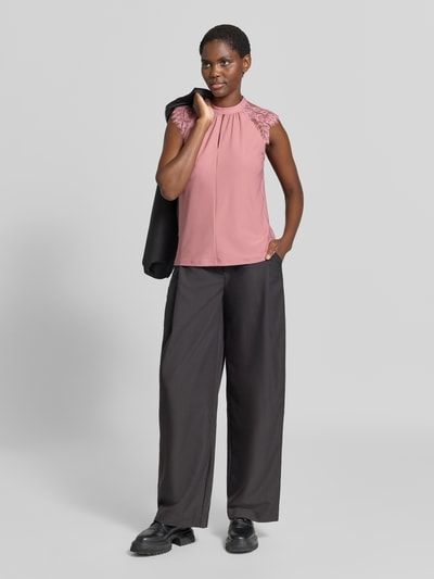 Frauenmodel trägt Regular Fit Kurzarmbluse mit semitransparenter Besatz Modell 'MILLA' von VERO MODA in Altrosa, kombiniert mit schwarzer weiter Hose, matter Stoff, legeres Design, Ganzkörperansicht von vorne.