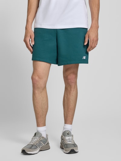 Męski model prezentuje Relaxed Fit Shorts mit Logo-Stitching von New Balance, mieszanka bawełny, elastyczny pas z tunelem, szerokość w rozmiarze M: 42 cm, długość wewnętrzna nogawki: 18 cm, widok całej sylwetki z przodu.