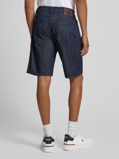 Männermodel trägt Bermudas im 5-Pocket-Design Modell 'Fort' von JOOP! Collection aus Baumwoll-Mix mit Stretch-Anteil in Dunkelblau, Ganzkörperansicht Rückansicht.