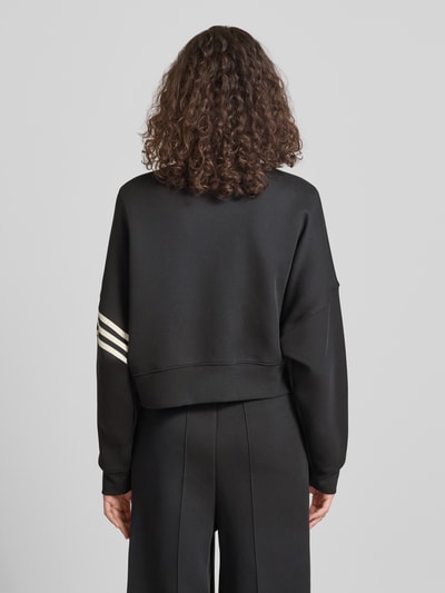 Kobiece modelka ma na sobie Regular Fit Sweatjacke aus Baumwoll-Mix od adidas Originals, czarny, gładki materiał sweat, długie rękawy z logo, stojący kołnierz, suwak, boczne kieszenie, bawełniany miks, widok całej sylwetki z tyłu.